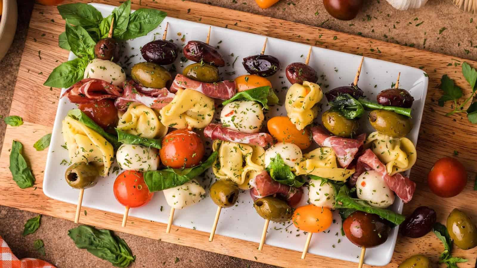 Skewers with mozzarella, tomatoes, tortellini, olives, basil, and cured meat on a white plate&mdash;perfect graduation party appetizers for your celebration.