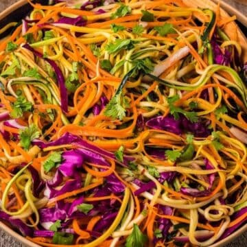 A bowl of colorful vegetable noodle salad with carrots, zucchini, purple cabbage, and fresh cilantro.