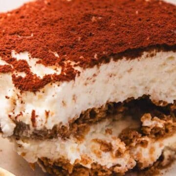 A slice of tiramisu dessert topped with cocoa powder on a plate with a gold-colored fork.