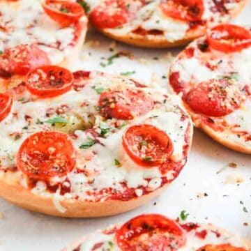 Bagels topped with melted cheese, tomato sauce, and pepperoni, garnished with herbs on a baking tray.