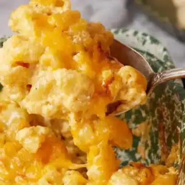 A spoon scooping cheesy, baked macaroni and cheese from a green and white dish evokes the comfort of vintage recipes enjoyed through generations.