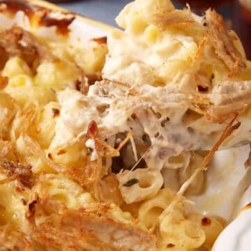 A close-up of creamy baked macaroni and cheese topped with shredded pulled pork being served from a dish—a delicious option for budget dinners.