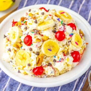 A bowl of banana split salad with whipped cream, banana slices, cherries, nuts, chocolate chips, and sprinkles.