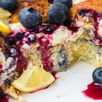 Baked French toast with blueberries, lemon slices, and berry sauce in a white dish with a serving missing—perfect for Easter breakfast casseroles.