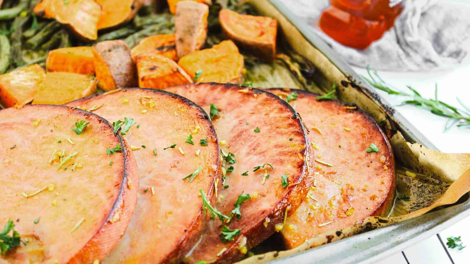 Slices of ham and chunks of sweet potato on a parchment-lined baking sheet, garnished with herbs.
