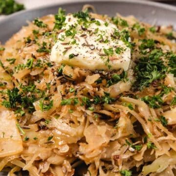 Shredded sautéed cabbage with herbs and a pat of butter on top, served on a gray plate.