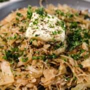 Close-up of sautéed cabbage topped with a pat of butter, fresh herbs, and seasonings on a plate.