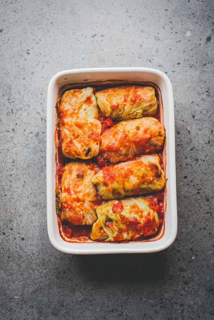 Six cabbage rolls topped with tomato sauce in a white baking dish on a gray textured surface, perfect for a classic Cabbage Rolls Casserole experience.
