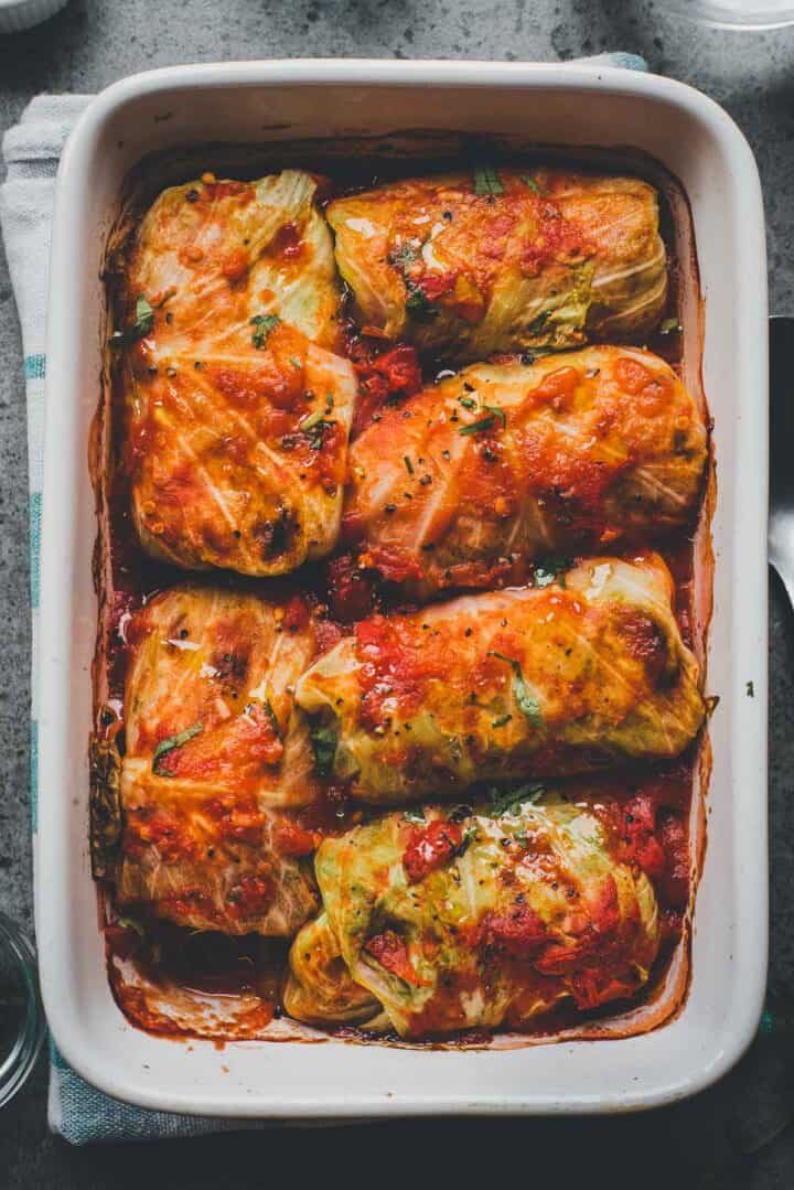 Six stuffed cabbage rolls topped with tomato sauce in a white baking dish, perfect for a classic Cabbage Rolls Casserole.