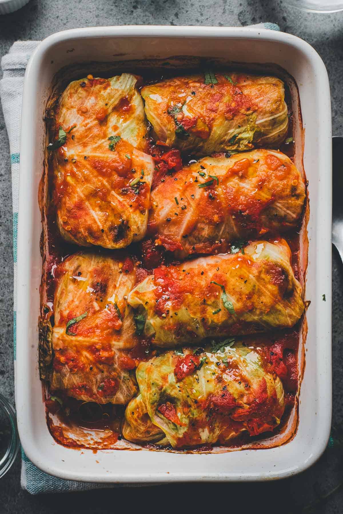 Six stuffed cabbage rolls topped with tomato sauce in a white baking dish, perfect for a classic Cabbage Rolls Casserole.