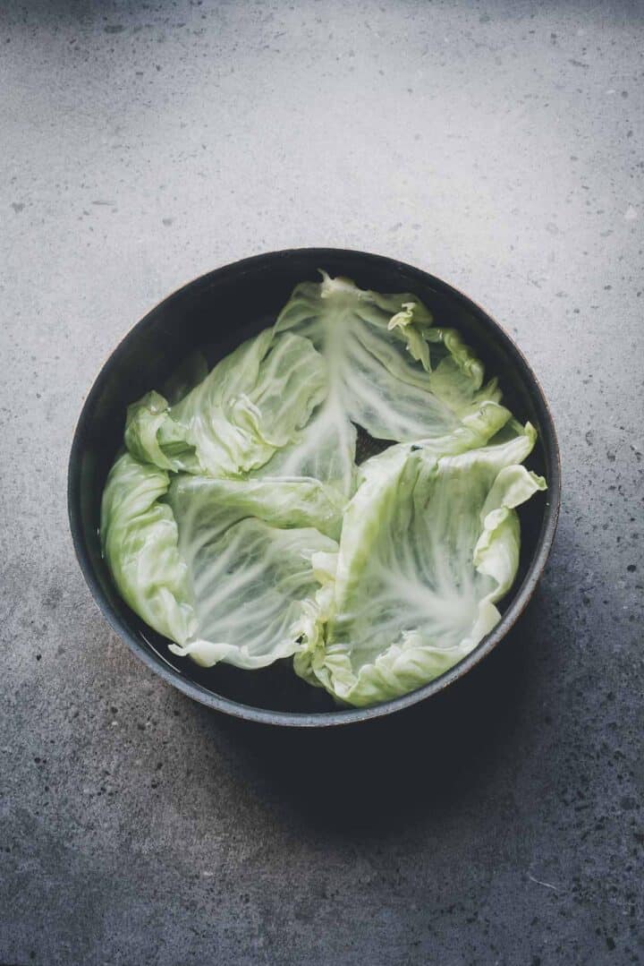 A bowl with several iceberg lettuce leaves, perfect for preparing dishes like Cabbage Rolls Casserole, sits on a gray textured surface.