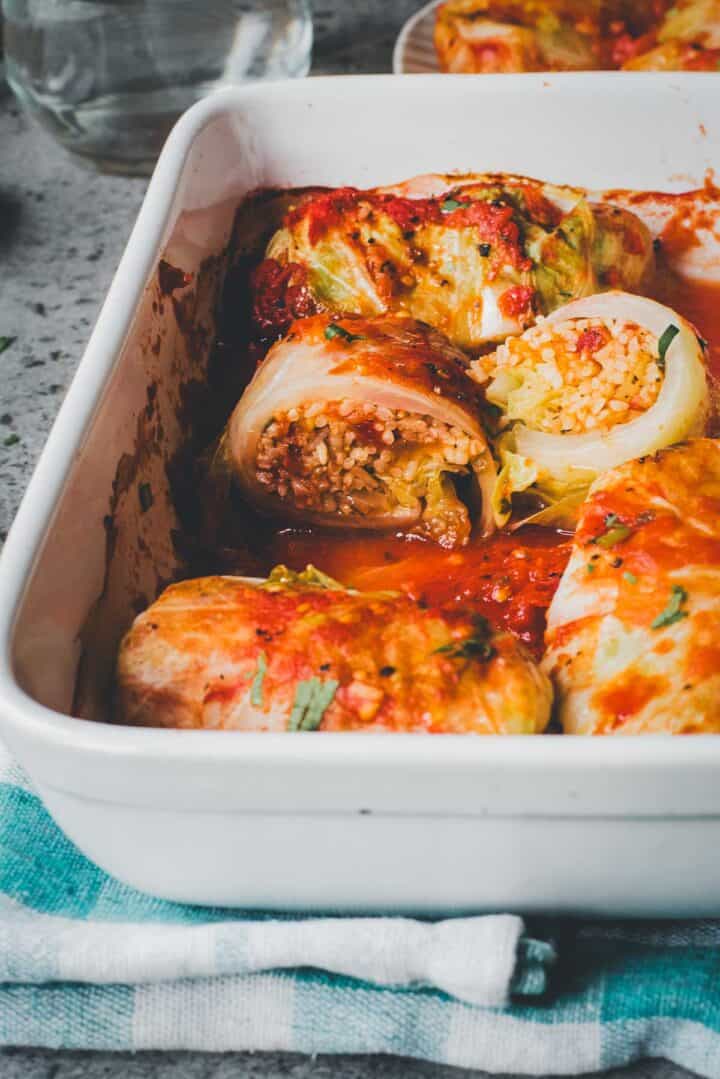 Cabbage Rolls Casserole in tomato sauce sits in a white baking dish atop a blue and white striped towel.