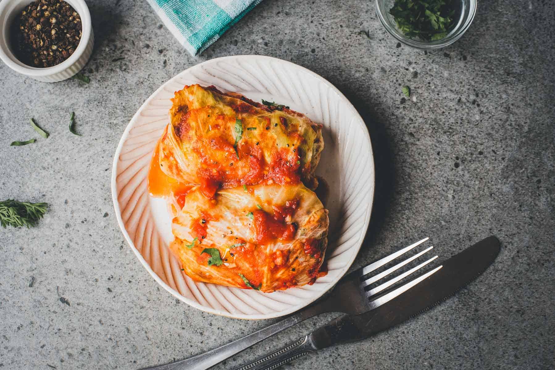 Two stuffed cabbage rolls topped with tomato sauce on a plate, served beside a fork and knife&mdash;just like your favorite Cabbage Rolls Casserole, but perfectly portioned for one.