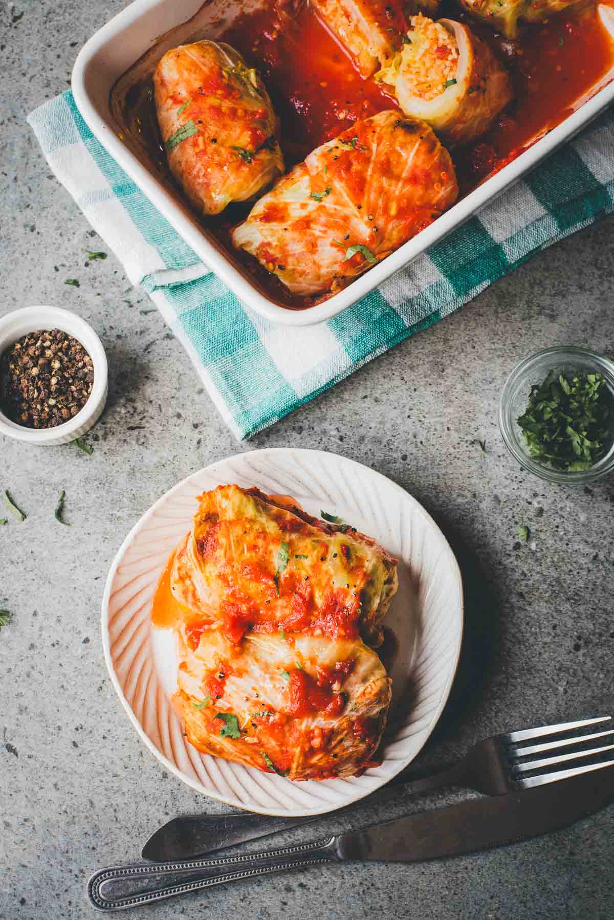 Two stuffed cabbage rolls topped with tomato sauce on a plate, with more Cabbage Rolls Casserole in a baking dish above.