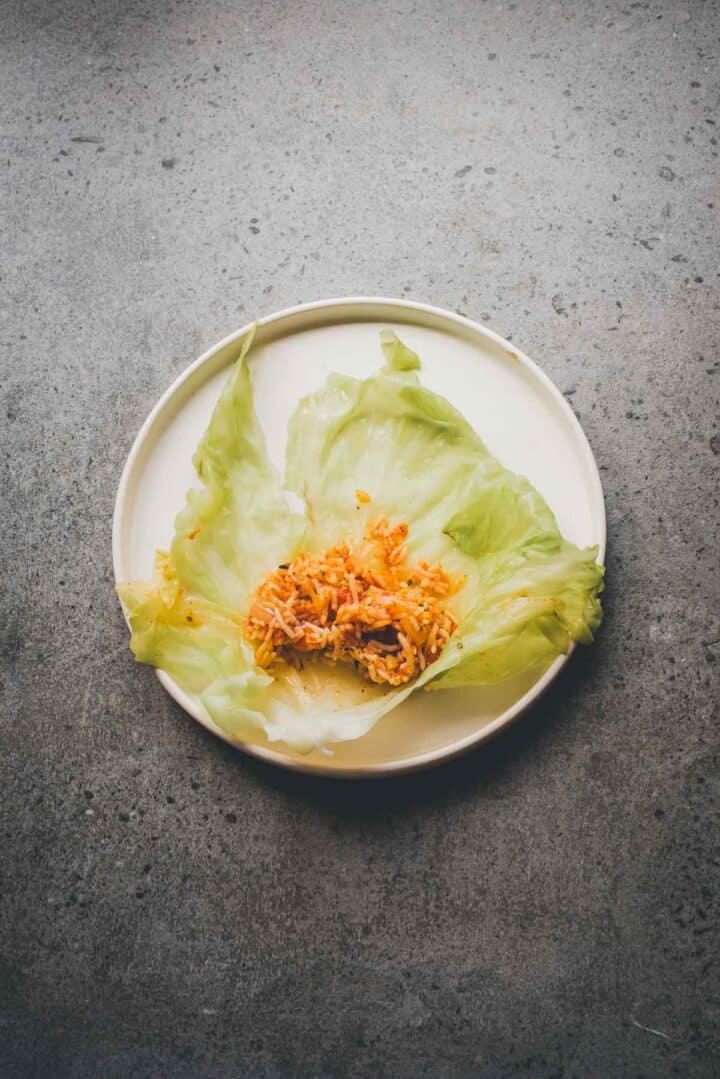A cabbage leaf on a plate filled with a small portion of rice and vegetables evokes the flavors of a classic Cabbage Rolls Casserole, set against a gray surface.