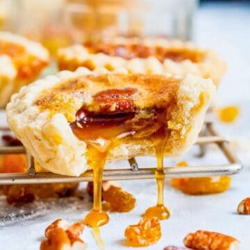 A butter tart with a bite taken out, gooey filling dripping, surrounded by nuts and raisins on a cooling rack.