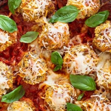 Baked meatballs with melted cheese and fresh basil on tomato sauce in a skillet.
