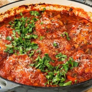 A casserole dish filled with chicken in tomato sauce, topped with chopped parsley and grated cheese—perfect for those craving World-Inspired Chicken Dinners.