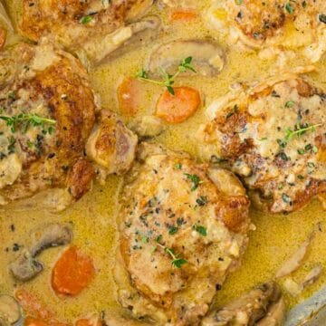Chicken thighs in creamy sauce with carrots, mushrooms, and fresh herbs in a skillet.