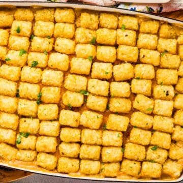 A casserole dish filled with tater tots arranged in neat rows, garnished with green herbs.