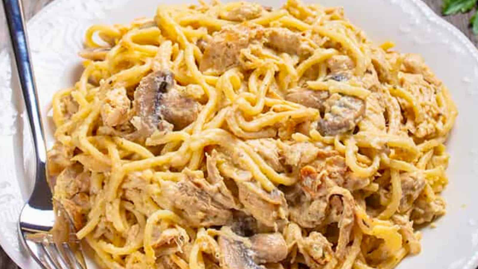 A plate of creamy chicken and mushroom pasta with a fork on the side.
