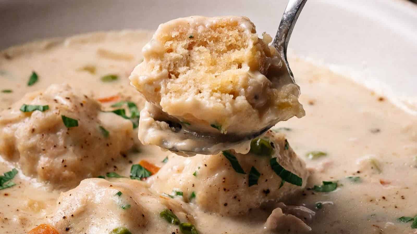 A spoon lifts a fluffy dumpling from creamy chicken and dumplings soup, garnished with fresh herbs&mdash;a comforting nod to classic depression-era recipes.