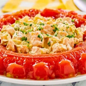 A molded ring of tomato aspic filled with a creamy chicken salad, garnished with chopped herbs on top.