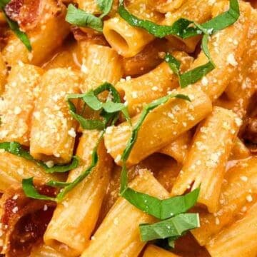 Creamy rigatoni pasta topped with tomato sauce, grated cheese, and fresh basil strips.