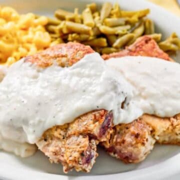 Plate with two pieces of chicken topped with white gravy, macaroni and cheese, and green beans.