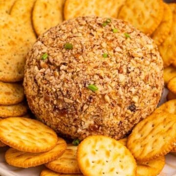 A classic cheese ball coated in nuts, surrounded by assorted round crackers on a white plate—one of those timeless retro appetizers perfect for any gathering.