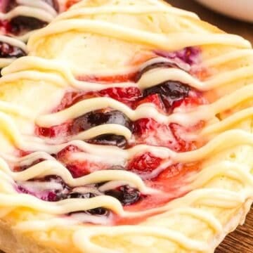 Two fruit danishes with icing drizzle on a wooden tray, topped with blueberries and red fruit filling—perfect as Easter desserts for your festive table.