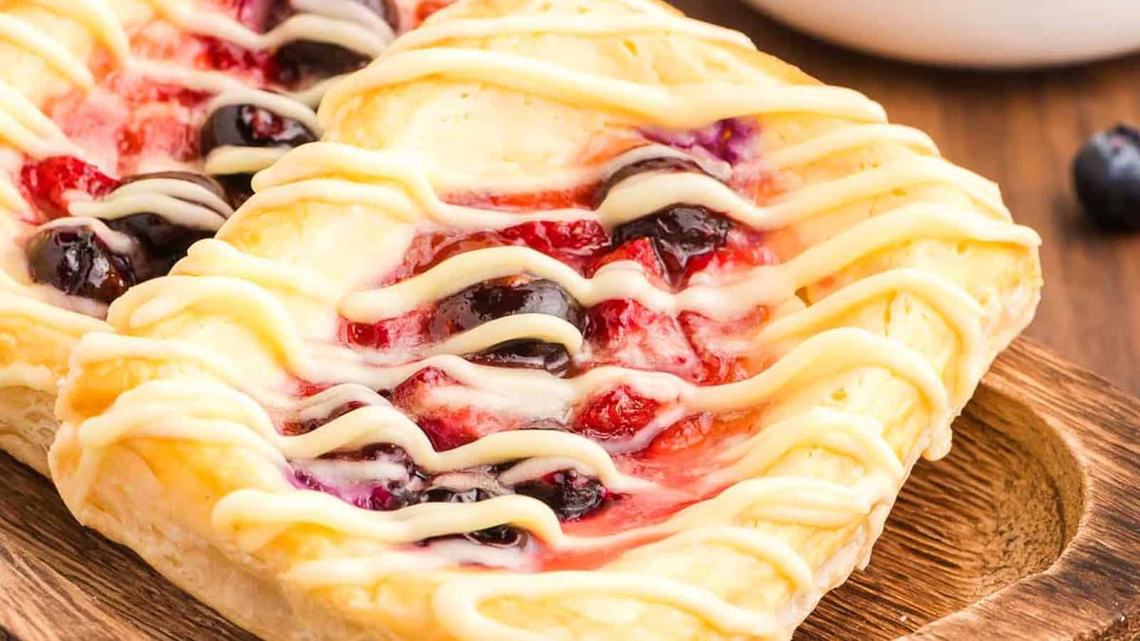 Two fruit danishes with icing drizzle on a wooden tray, topped with blueberries and red fruit filling&mdash;perfect as Easter desserts for your festive table.
