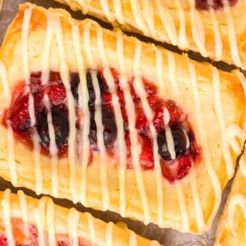 Rectangular fruit danishes with berry filling and white icing drizzle on a parchment-lined surface—perfect as festive Easter desserts.