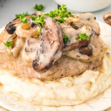Mashed potatoes topped with a pork chop, creamy mushroom sauce, and fresh parsley on a white plate—a classic nod to old-fashioned dinners.