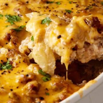 Classic Potluck Favorite: Cheesy casserole topped with ground meat and herbs, with a serving being scooped out of a white dish.