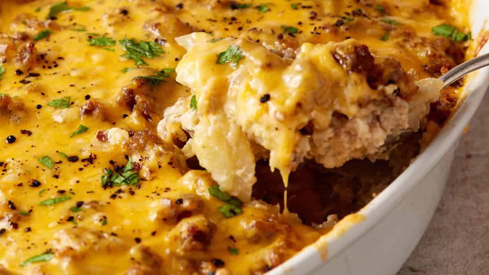 Classic Potluck Favorite: Cheesy casserole topped with ground meat and herbs, with a serving being scooped out of a white dish.