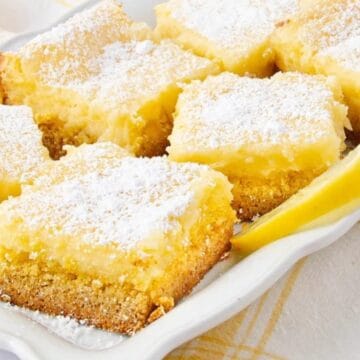 Lemon bars dusted with powdered sugar on a white tray, garnished with lemon slices—perfect as easy potluck desserts everyone will love.