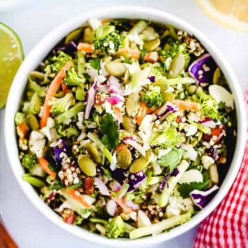 Bowl of colorful chopped salad with seeds, vegetables, lime, and utensils beside a red-striped napkin.