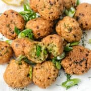 Golden-brown fried falafel balls garnished with chopped green onions and dill on a white surface.