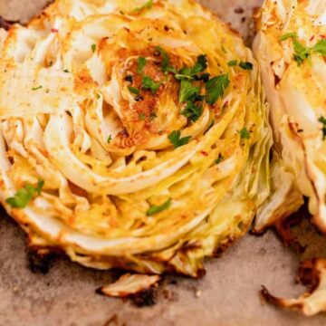 Close-up of roasted cabbage steaks topped with chopped herbs on parchment paper.