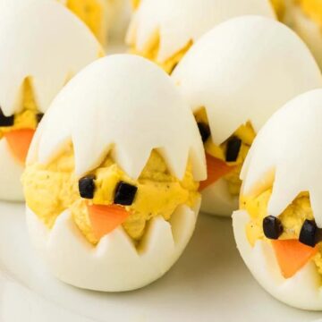 Deviled eggs decorated to look like baby chicks hatching, with carrot beaks and olive eyes.