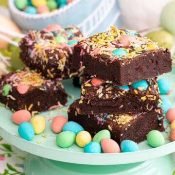 Chocolate brownies topped with colorful sprinkles and candies, stacked on a plate with candy eggs around them.