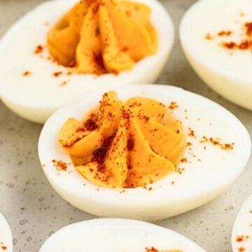 Deviled eggs with a creamy filling, topped with paprika, arranged on a light-colored surface.