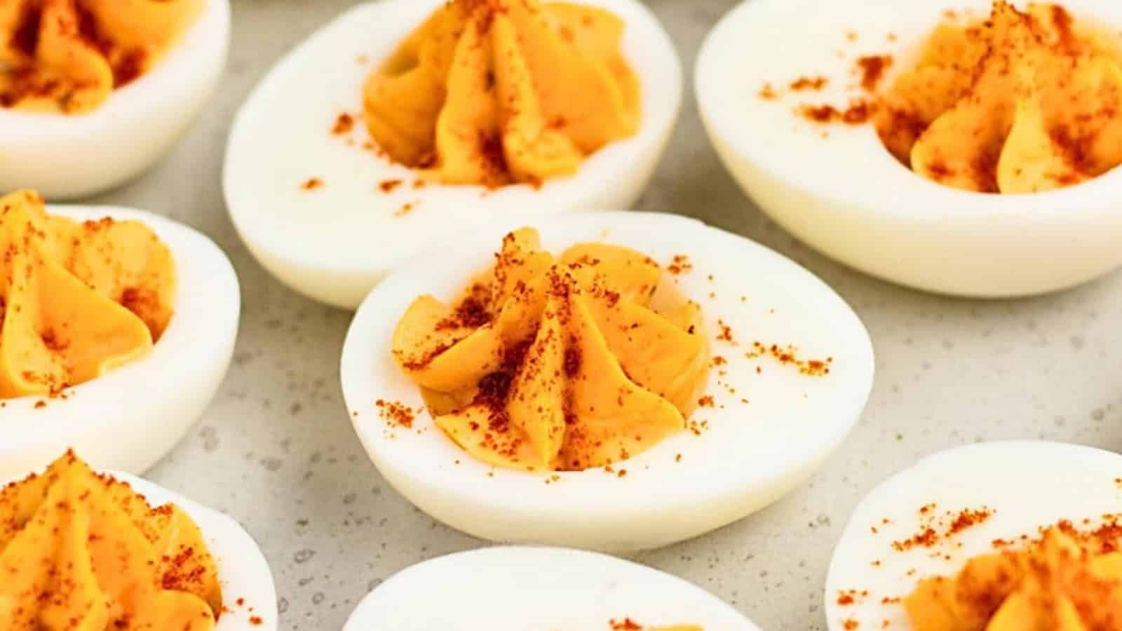 Deviled eggs with a creamy filling, topped with paprika, arranged on a light-colored surface.