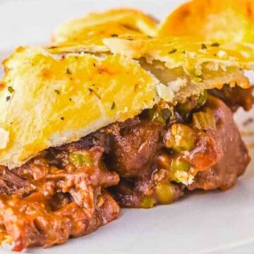 A slice of savory meat pie with a golden, flaky crust on a white plate.