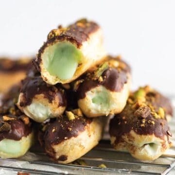 A stack of chocolate-covered eclairs filled with green pistachio cream on a cooling rack.