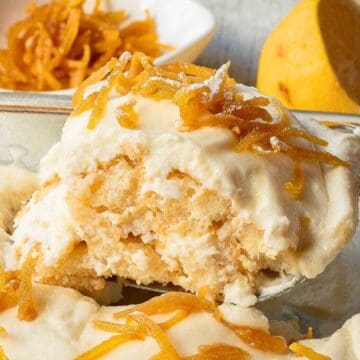 A creamy lemon dessert topped with lemon zest is being served from a glass dish.