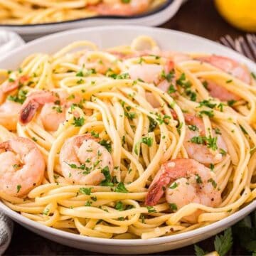 A bowl of shrimp pasta garnished with parsley, with lemons and forks on the side—perfect for those seeking delicious lent-friendly recipes.
