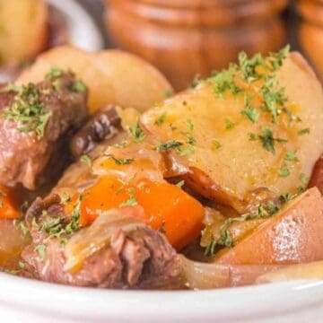Beef stew with potatoes, carrots, and parsley served in a white bowl.
