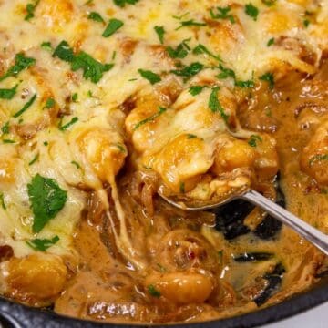 Cheesy baked gnocchi in a skillet with herbs, sauce, and a spoon scooping a serving.